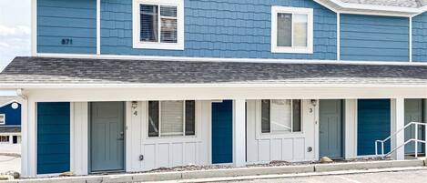 A two-story building with a blue exterior and white trim, featuring a covered front porch with four doors and windows.