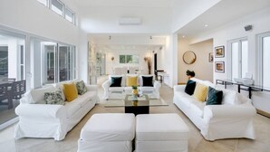 A spacious living room with white furniture, a coffee table, and a dining area in the background. - Lake View: Lake/golf view villa with full staff, pool, Jacuzzi & pool table (Punta Cana)