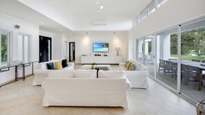 A spacious living room with a large white sectional sofa, a coffee table, and a flat-screen TV mounted on the wall. - Lake View: Lake/golf view villa with full staff, pool, Jacuzzi & pool table (Punta Cana)