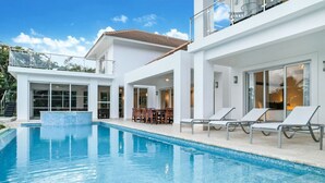 A modern poolside area with a clear blue pool, lounge chairs, and a dining area with outdoor furniture. - Lake View: Lake/golf view villa with full staff, pool, Jacuzzi & pool table (Punta Cana)