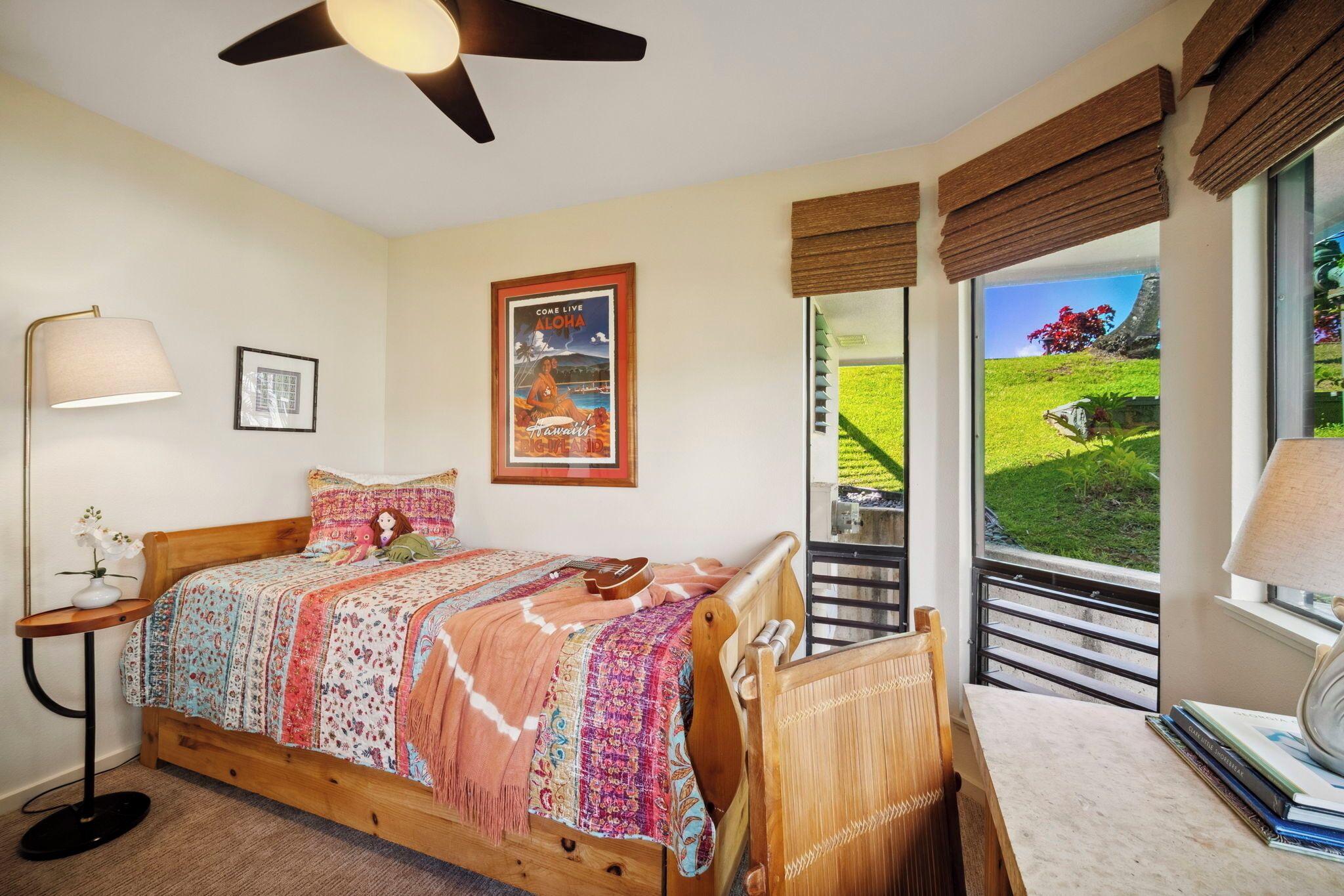 A bedroom with a wooden bed, a nightstand, a lamp, a poster, and a view of a green landscape through a window.