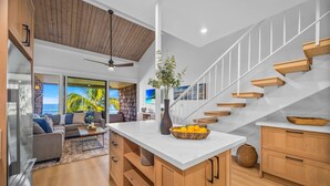 A modern kitchen with a white countertop, wooden cabinets, and a staircase with white railings. - Beachfront 2BD Unobstructed Ocean Views - Kulakane 304 (Lahaina)