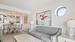 A modern living room with a grey sofa, wooden coffee table, and a dining area with a white table and chairs. - Last Minute Rate, Direct Oceanfront 4BR/3BA, Sleep 16, Central Location (Myrtle Beach)