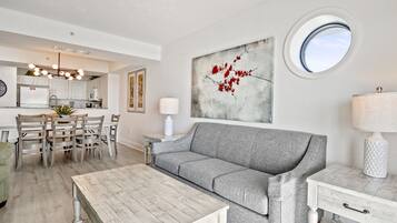 Una sala moderna con un sofá gris, una mesa de centro de madera y un comedor con una mesa y sillas blancas.