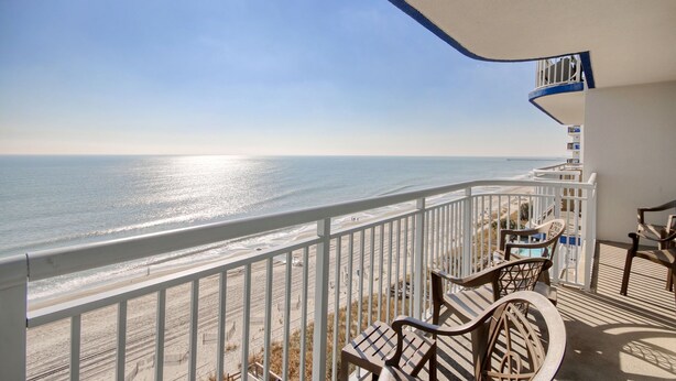 A balcony with a view of the ocean, wooden chairs, and a white railing. - Last Minute Rate, Direct Oceanfront 4BR/3BA, Sleep 16, Central Location (Myrtle Beach)