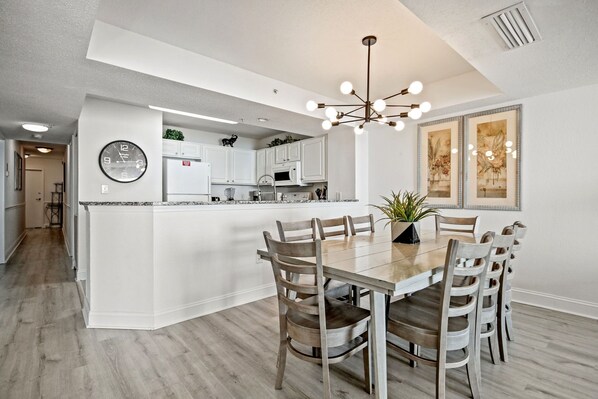 Une cuisine moderne avec des meubles blancs, un îlot central et un coin repas doté de chaises en bois.