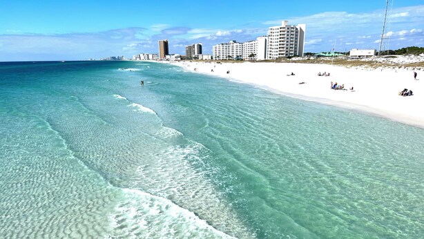 A beach with clear turquoise water, white sand, and a city skyline in the background.