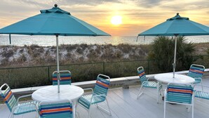 A deck with outdoor seating and umbrellas overlooking a beach.
