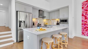 A modern kitchen with grey cabinets, a stainless steel refrigerator, a microwave, and a large island with bar stools.