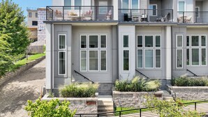 A modern multi-story residential building with a balcony, large windows, and a stone pathway leading to the entrance.