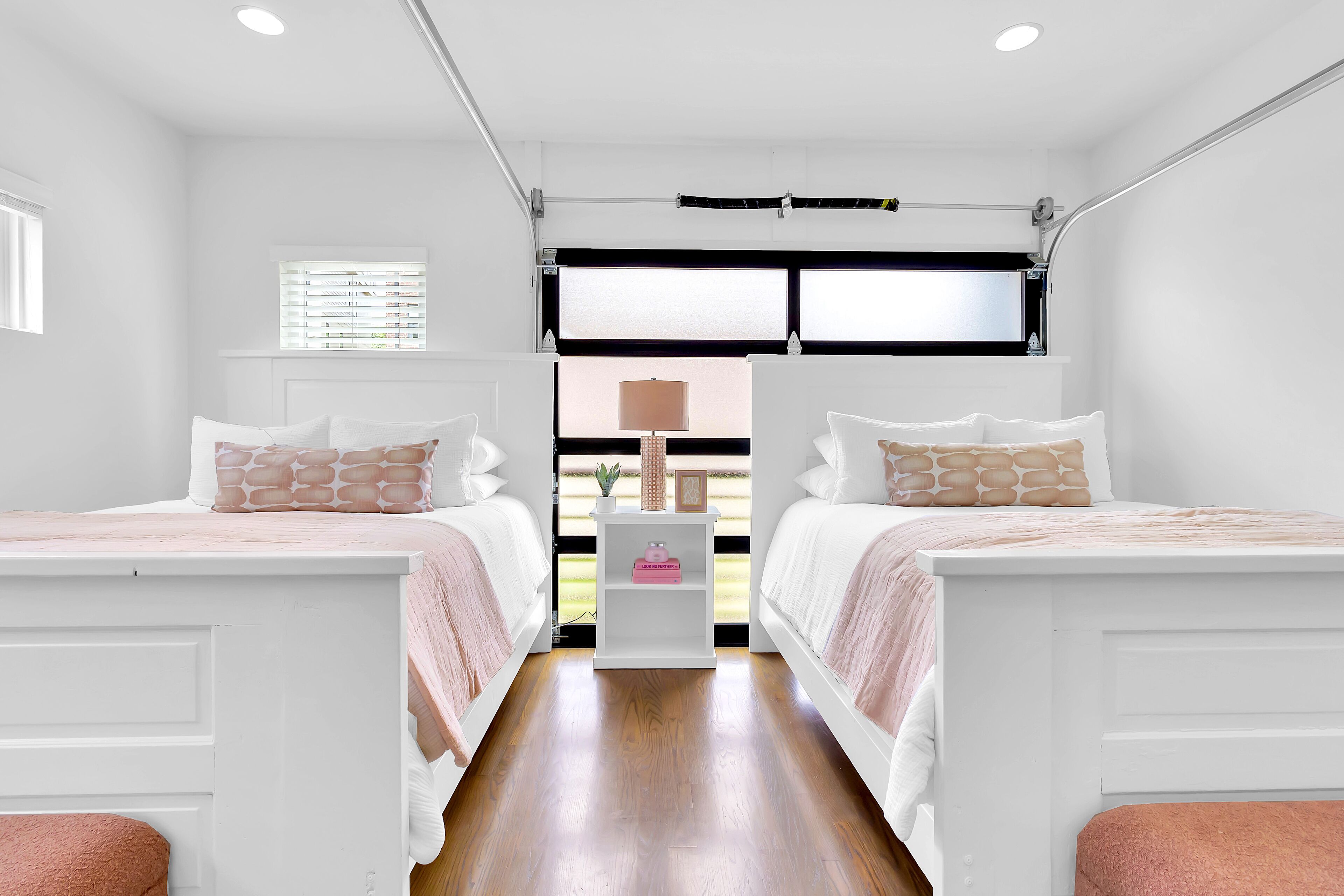 Een slaapkamer met twee bedden, een witte kledingkast, een nachtkastje en een raam met zonwering.