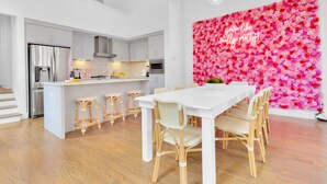 A modern kitchen with white cabinetry, a central island, and a dining area with a white table and wicker chairs.