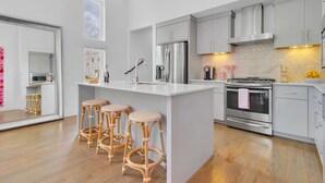 A modern kitchen with white cabinetry, a stainless steel refrigerator, a built-in oven, and a large island with bar stools.