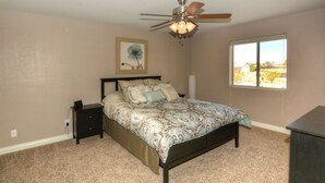 A bedroom with a bed, a nightstand, a ceiling fan, a window with a view, and a wall-mounted artwork. - Beautiful home with 2 masters! (Lake Havasu City)