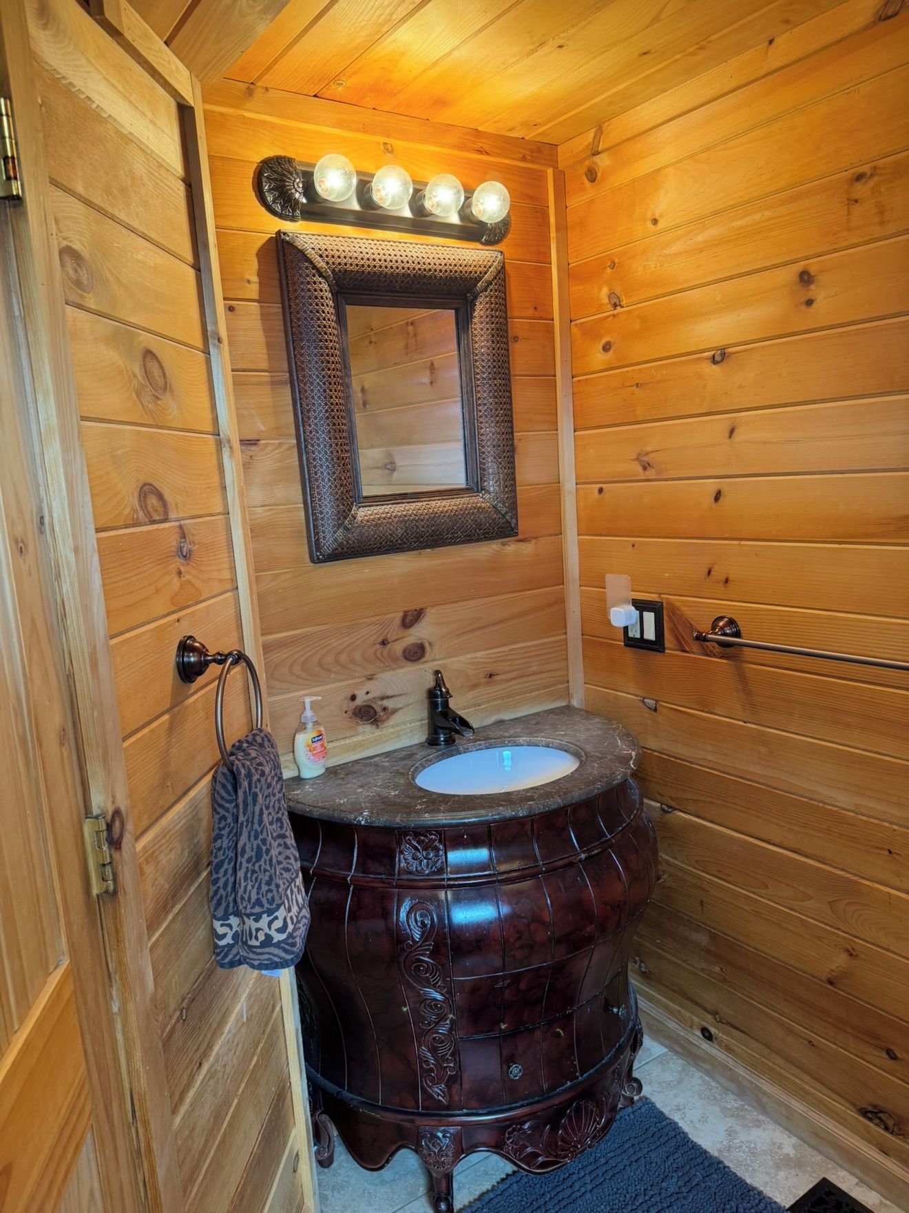 Een badkamer met houten lambrisering, een rond, donker houten wastafelmeubel, een spiegel met verlichting erboven en een handdoekhouder.