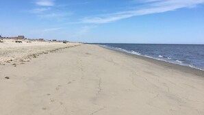 A wide, empty beach with a clear sky and calm sea. - Steps from beach access, family friendly home with all the amenities! (Milton)