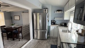 A modern kitchen with a stainless steel refrigerator, a dining area with a wooden table and chairs, and a window providing natural light. - Steps from beach access, family friendly home with all the amenities! (Milton)