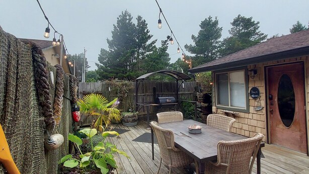 A patio with a wooden table and wicker chairs, surrounded by potted plants and a stone wall.
