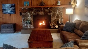 A cozy living room with a stone fireplace, wooden walls, a leather couch, and a coffee table.
