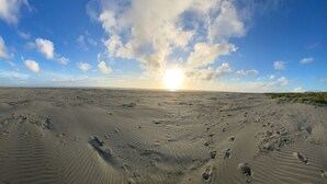A wide sandy beach with footprints and a clear sky with clouds.