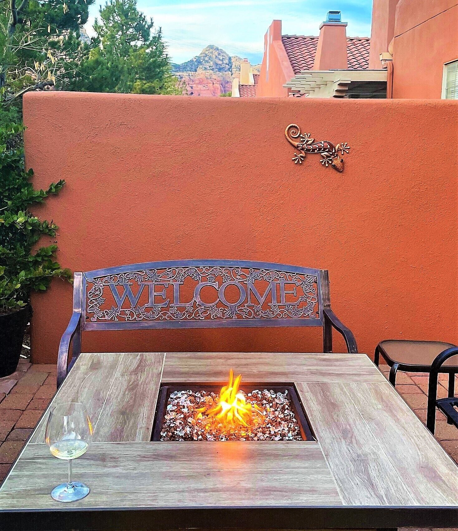 A patio with a metal bench, a fire pit, and a 'WELCOME' sign.
