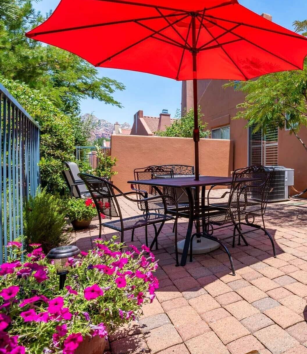 Eine Terrasse im Freien mit einem roten Sonnenschirm, Metallstühlen, einem Tisch und Topfpflanzen.