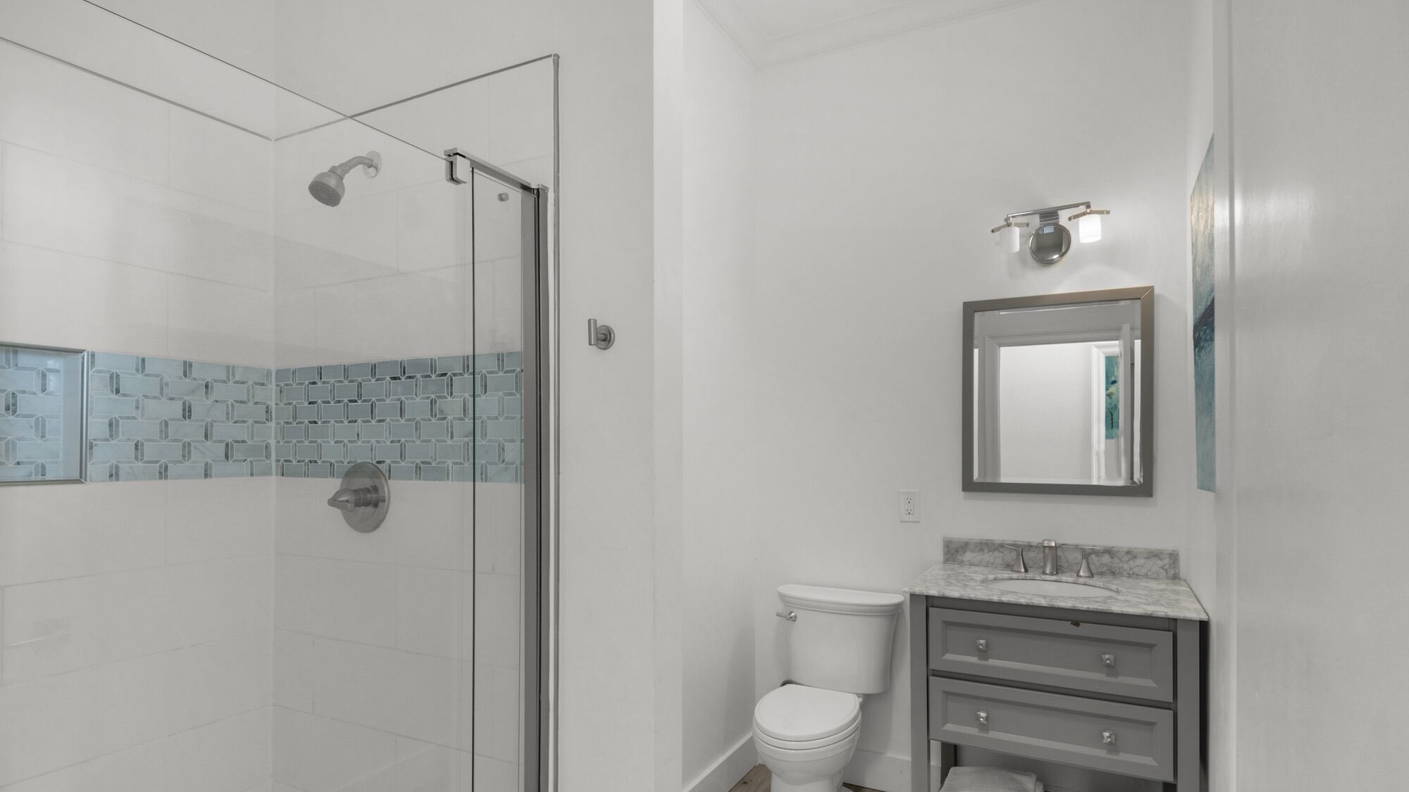 A bathroom with a glass shower enclosure, a toilet, and a vanity with a mirror.