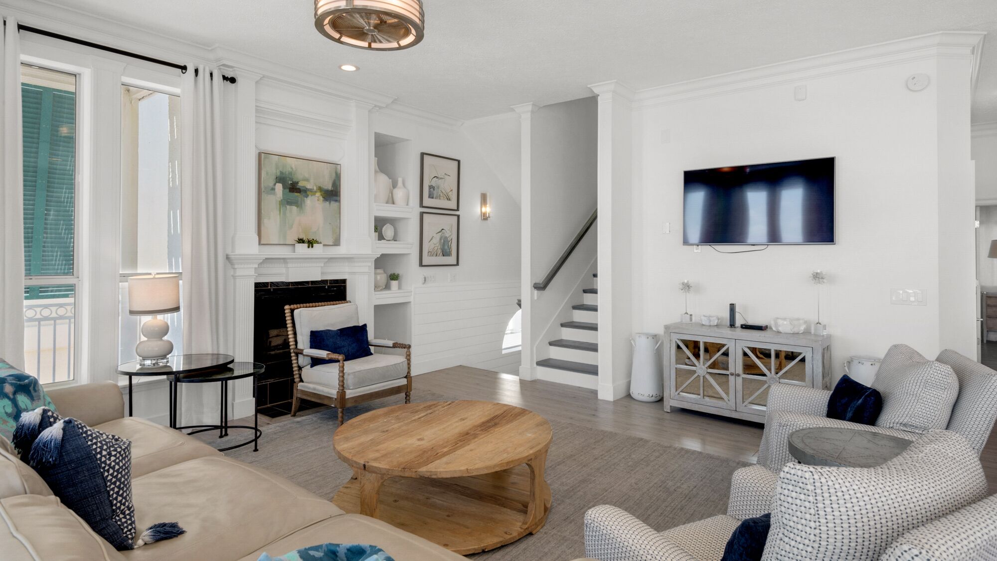 A spacious living room with a fireplace, a staircase, and a television mounted on the wall.