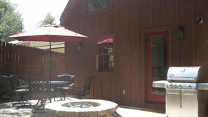 Une terrasse extérieure avec un foyer en pierre, un barbecue et un espace repas comprenant des chaises et une table.
