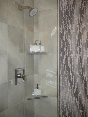 Een douche met handdouche, een wastafel met glazen ombouw en een betegelde wand met een verticaal patroon.