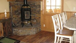Une pièce chaleureuse avec une cheminée en pierre, un plancher en bois et un coin repas avec des chaises blanches.