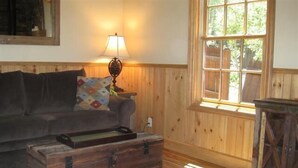 Une pièce aux murs lambrissés, avec un canapé, une lampe, une fenêtre et une commode en bois.
