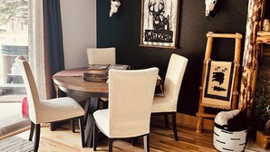 Un comedor con una mesa redonda de madera, cuatro sillas tapizadas y una pared oscura con cráneos de ciervo montados y un letrero de bienvenida.