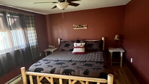Un dormitorio con cama, ventilador de techo, mesita de noche, lámpara y ventana con cortinas.
