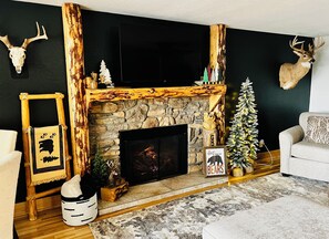 A cozy living room with a stone fireplace, a mounted deer head, and a Christmas tree.