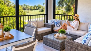 A sunlit outdoor seating area with wicker furniture, a table, and potted plants.