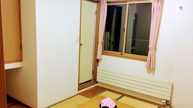 A room with a sliding door, a window with curtains, a radiator, a tatami mat floor, and a small table with a pink cloth. - Minshuku Sumitomo (Hakodate)