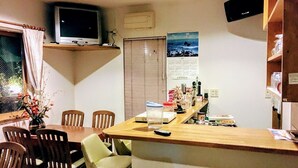 A compact living space with a dining area, a small kitchen counter, and a television mounted on the wall. - Minshuku Sumitomo (Hakodate)
