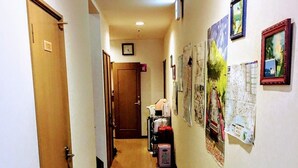 A hotel hallway with wooden flooring, a door labeled "102", and various framed pictures on the walls. - Minshuku Sumitomo (Hakodate)