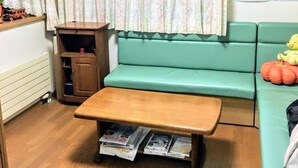 A corner room with a wooden bench, a green sofa, a wooden cabinet, and a window with curtains. - Minshuku Sumitomo (Hakodate)
