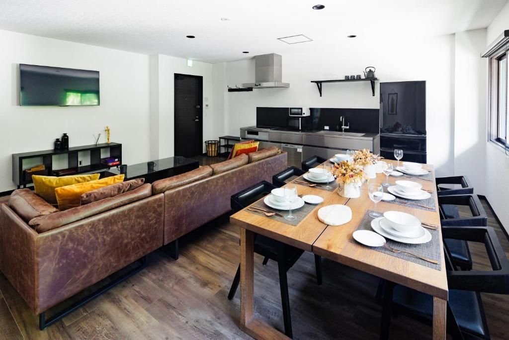 Una cocina moderna con horno empotrado y microondas, un comedor con mesa de madera dispuesta para cuatro personas, y un sofá de cuero marrón con cojines amarillos.