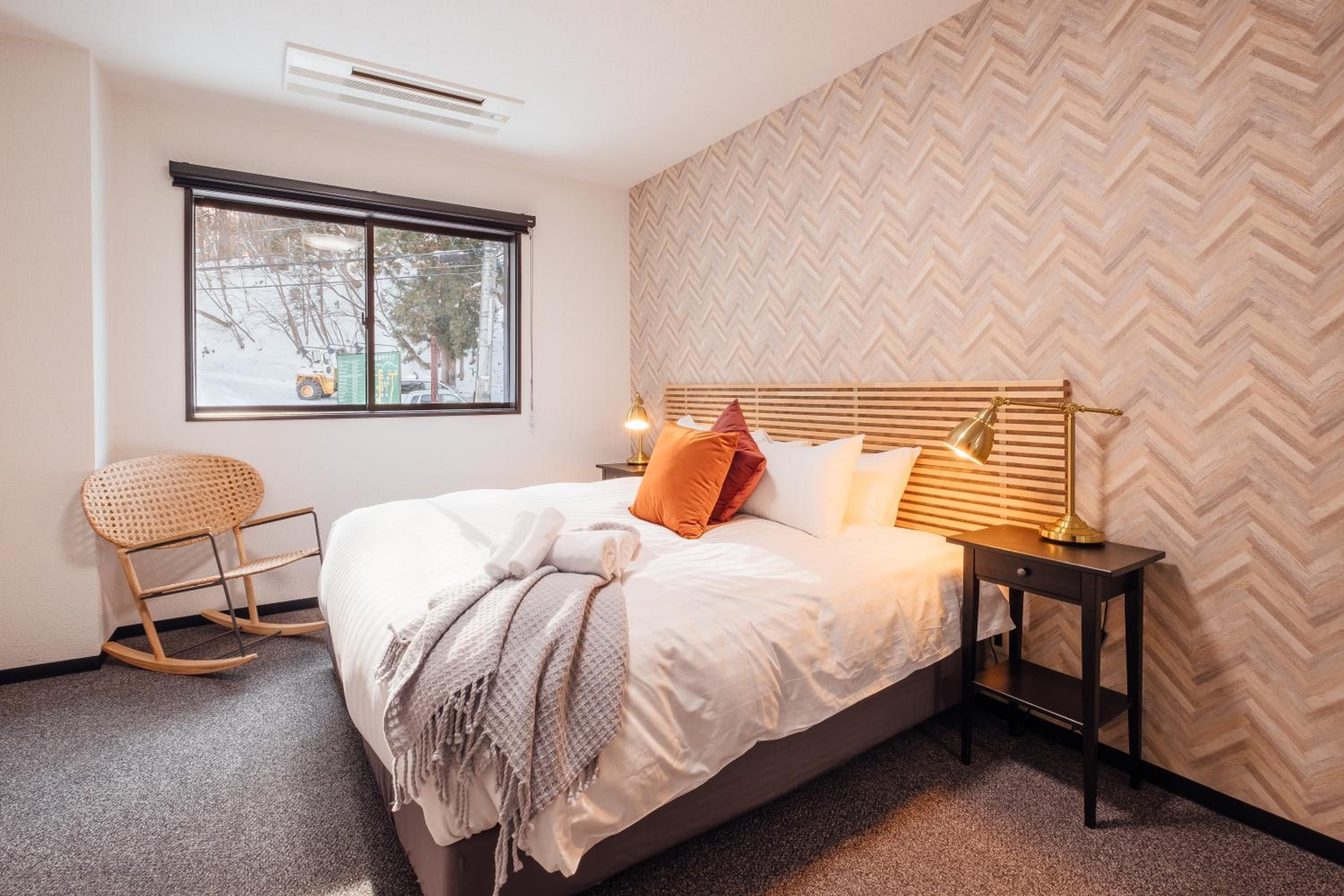 A hotel room with a bed, a window, a chair, and a nightstand.