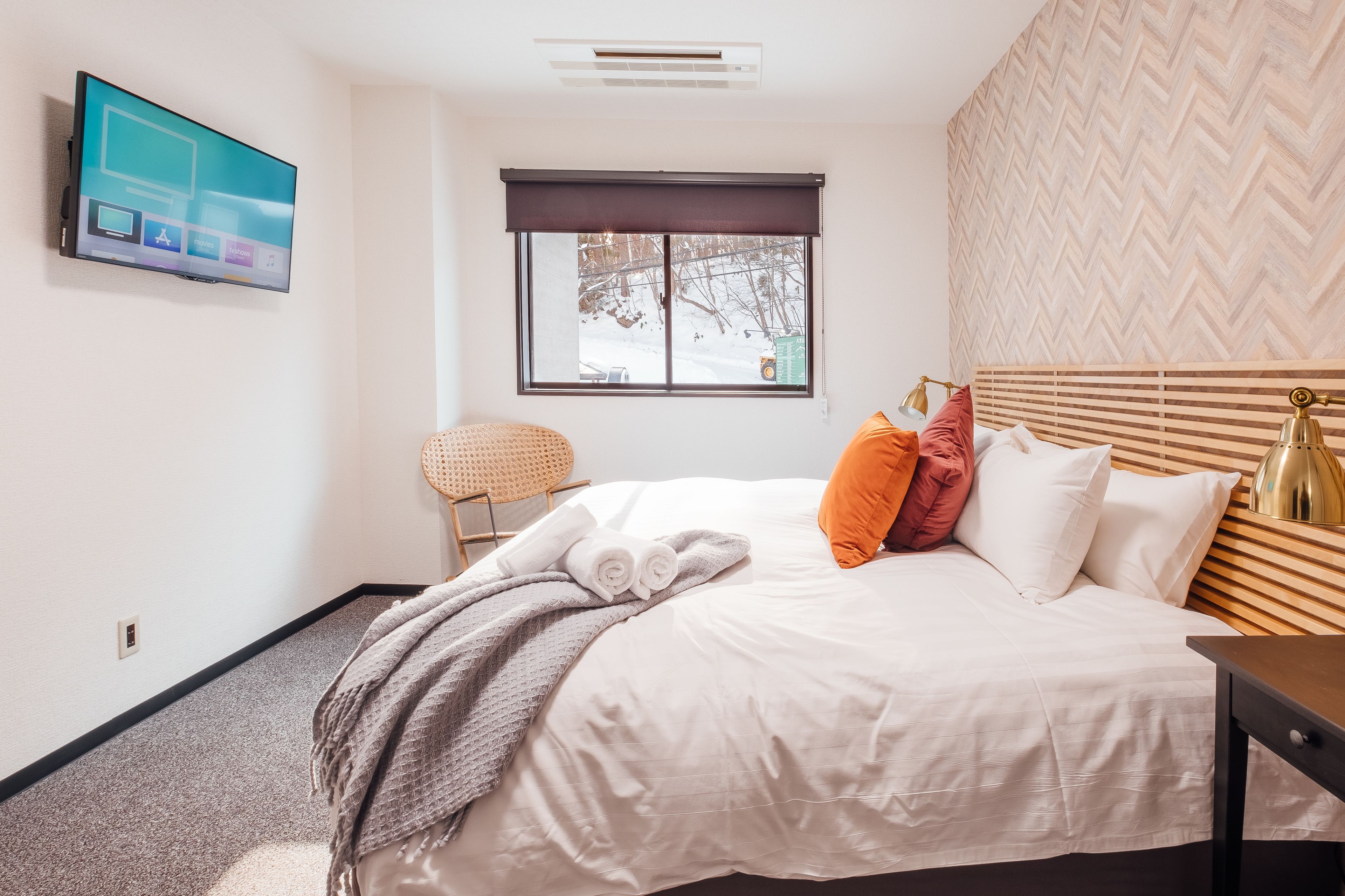 Habitación de hotel con cama, televisión montada en la pared, ventana con vistas al exterior y cabecero de madera.