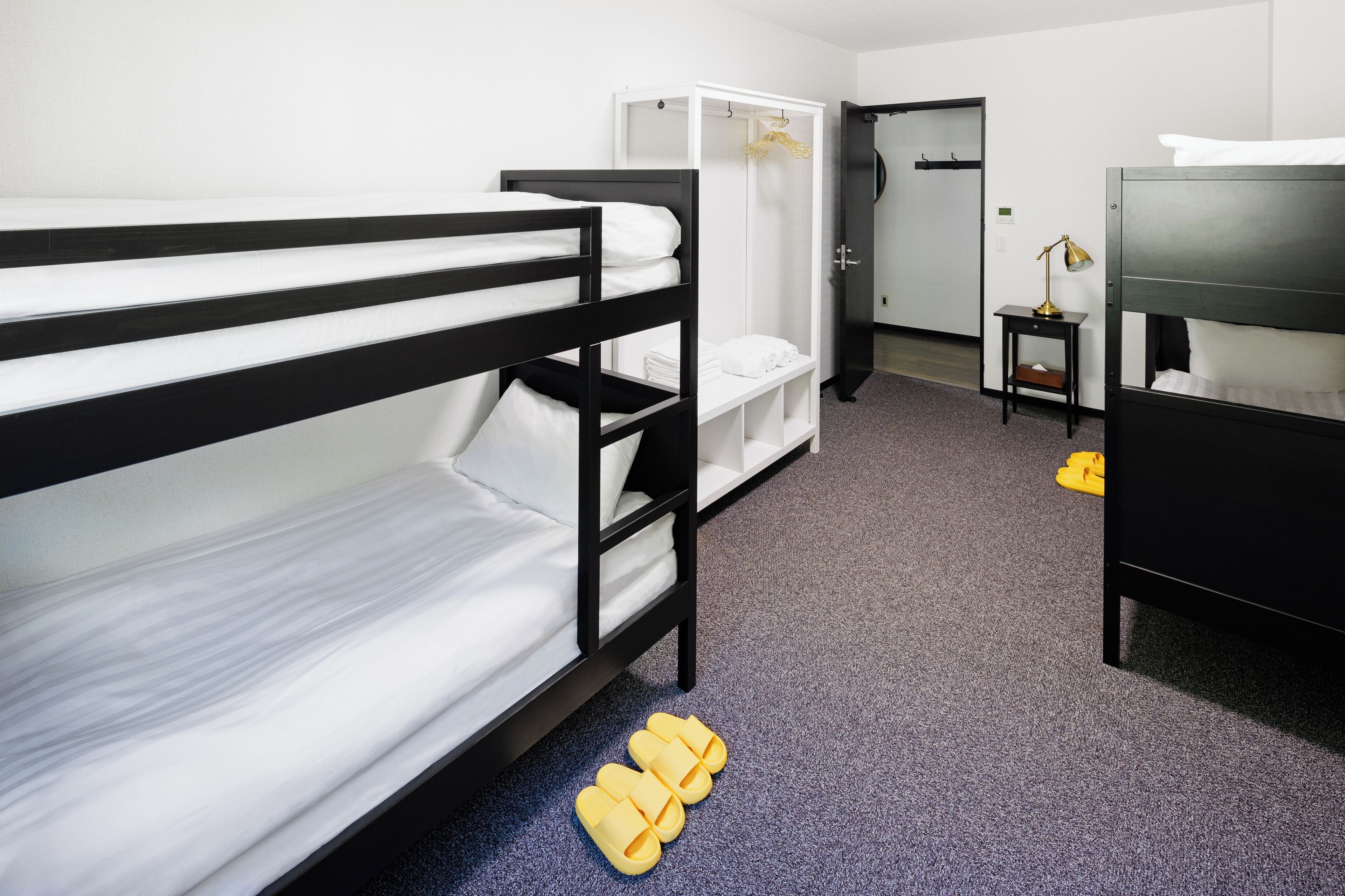 A bunk bed room with a wardrobe, a desk with a lamp, and a door leading to another room.