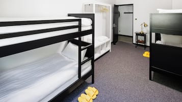 A bunk bed room with a wardrobe, a desk with a lamp, and a door leading to another room.
