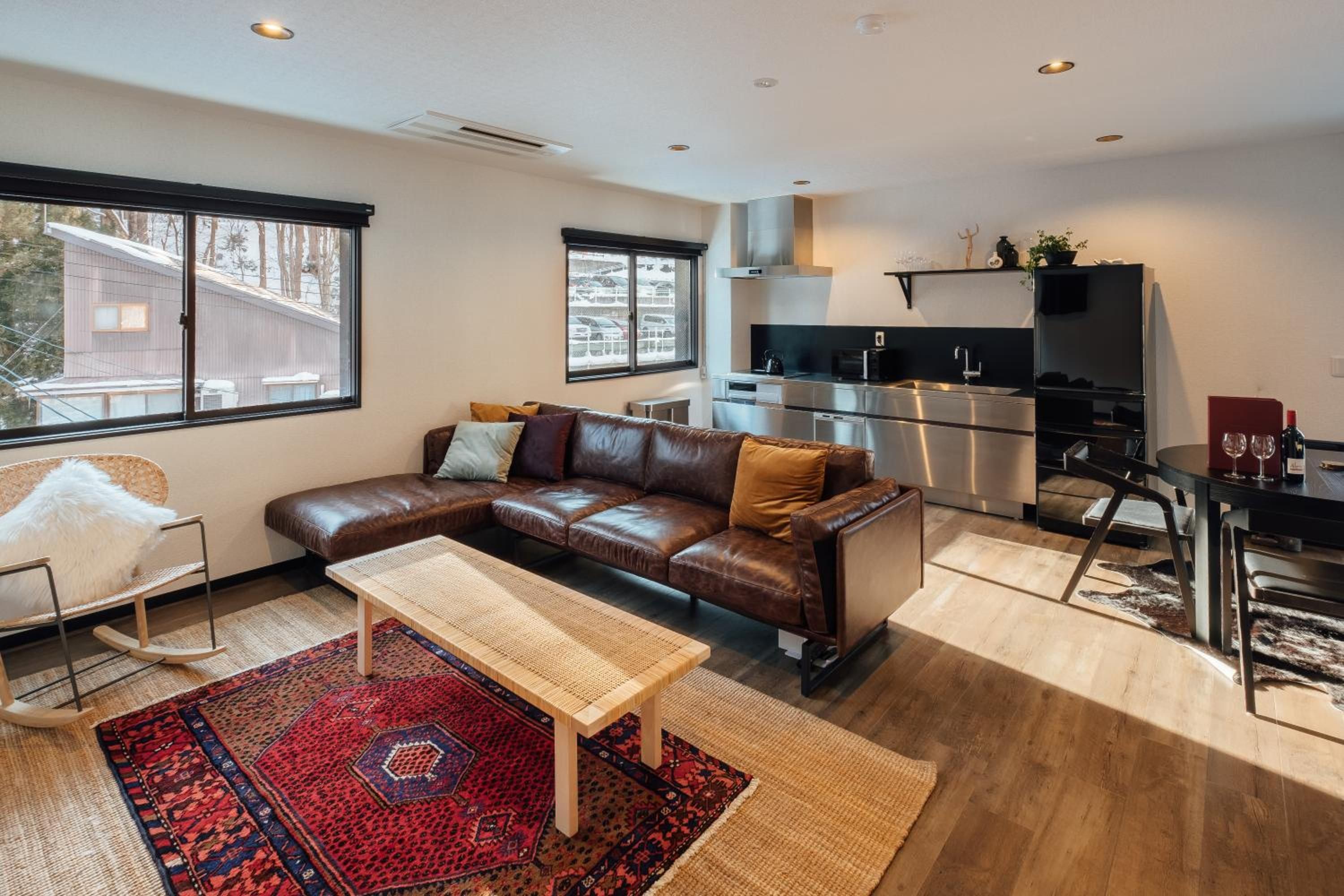 A modern living room with a brown leather sofa, a wooden coffee table, and a red patterned rug.