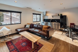 A modern living room with a brown leather sofa, a wooden coffee table, and a red patterned rug. - Happo Apartments (Hakuba)