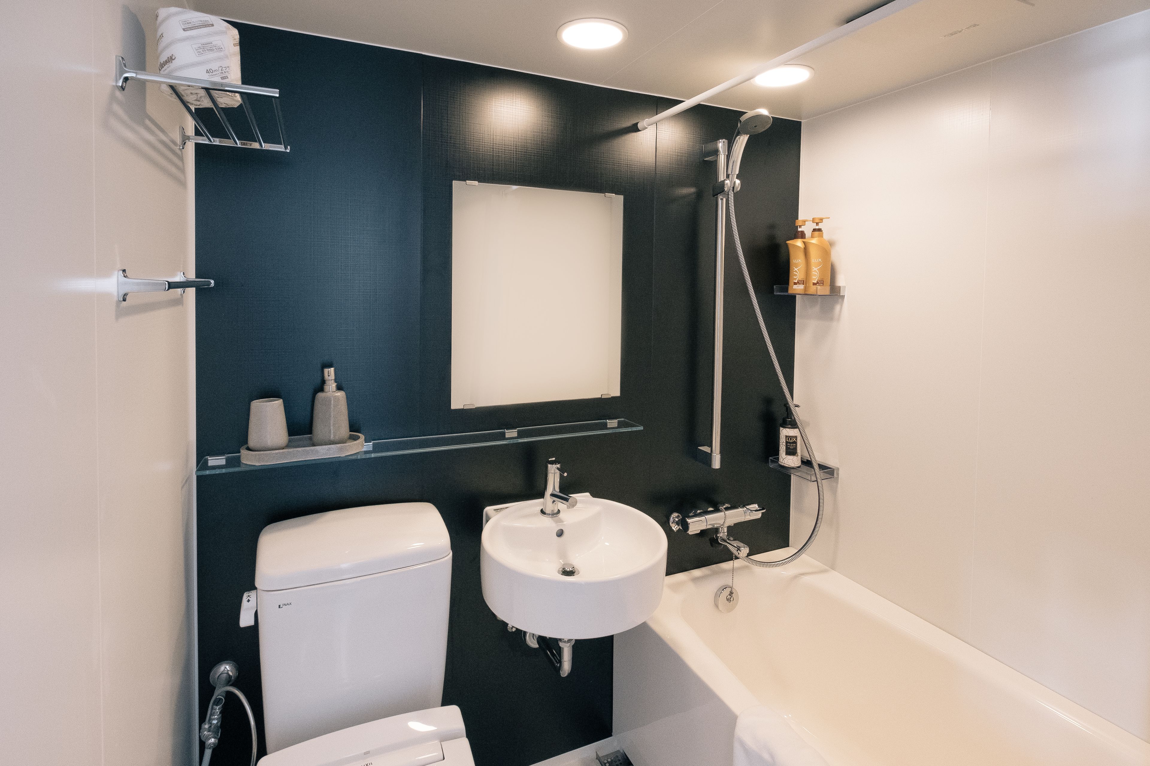 Een moderne badkamer met toilet, wastafel en bad. Een plank met toiletartikelen en een handdoekrek zijn aanwezig.