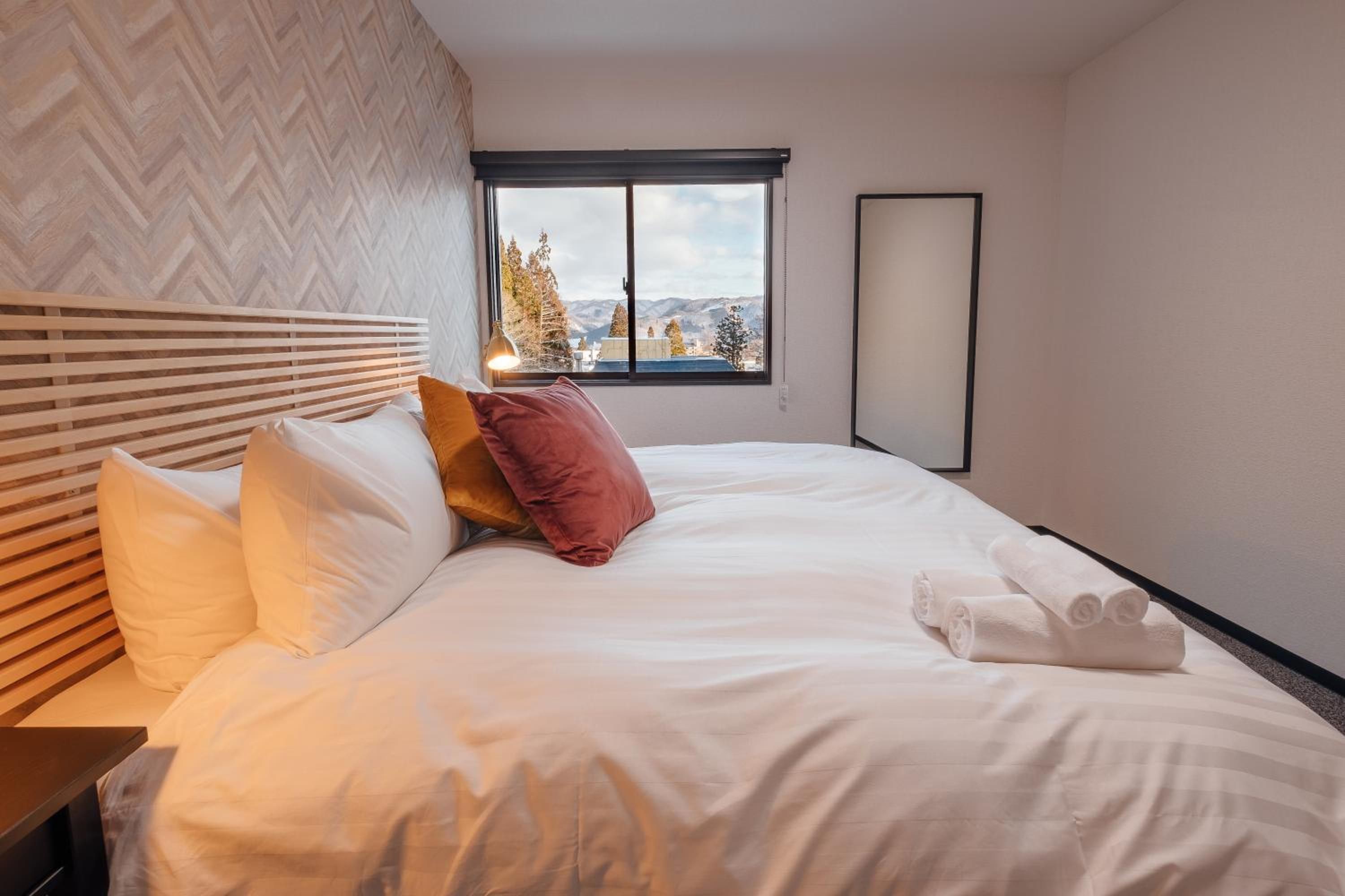 A hotel room with a bed, a nightstand, a window with a view of trees and mountains, and a wall-mounted mirror.