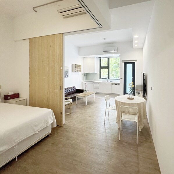Una habitación de hotel moderna con cama, una zona de comedor con mesa y sillas, un sofá y una cocina al fondo.
